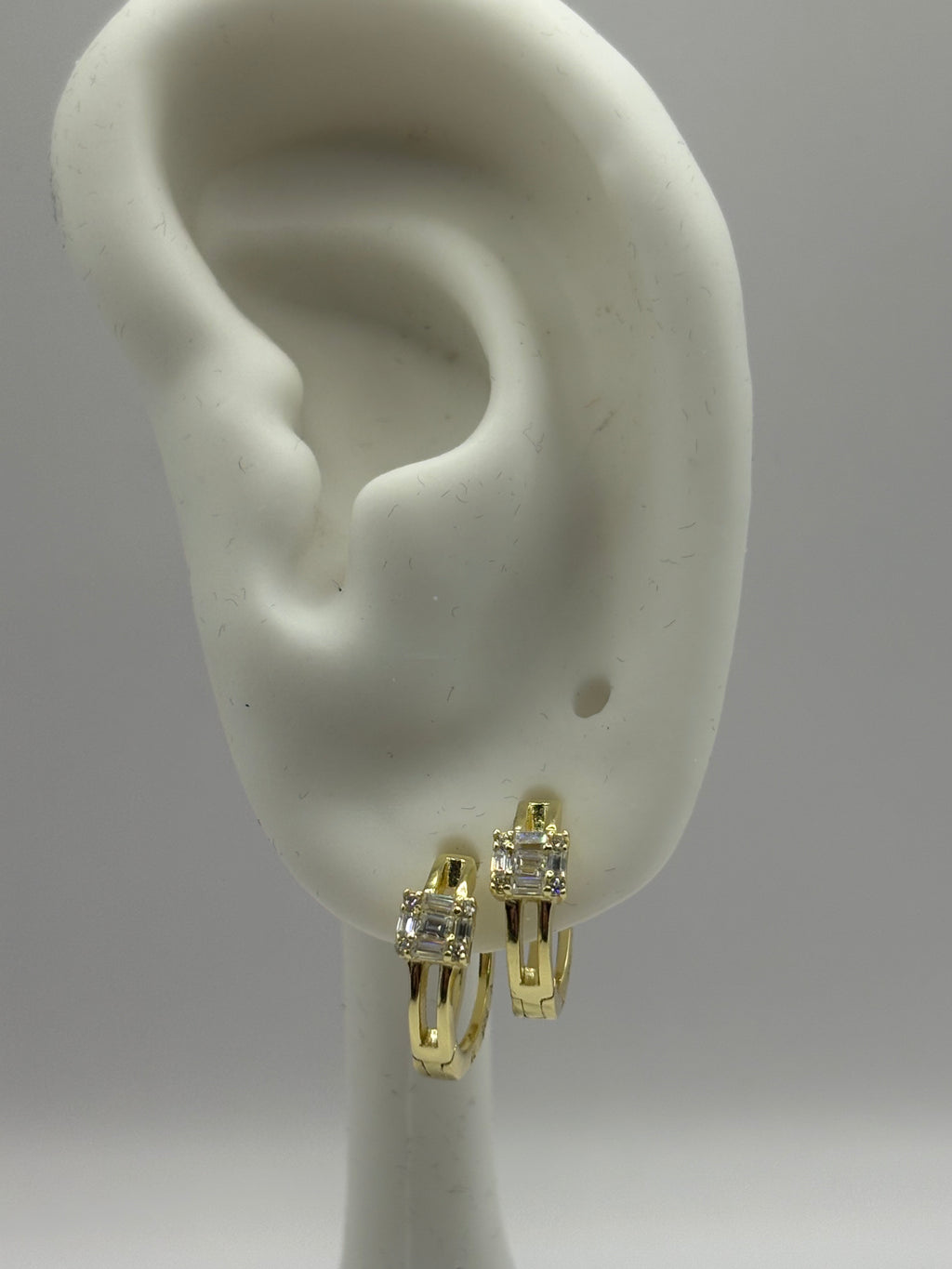 Huggie hoop earrings feature a distinctive open split-shank band and a geometric moissanite cluster design