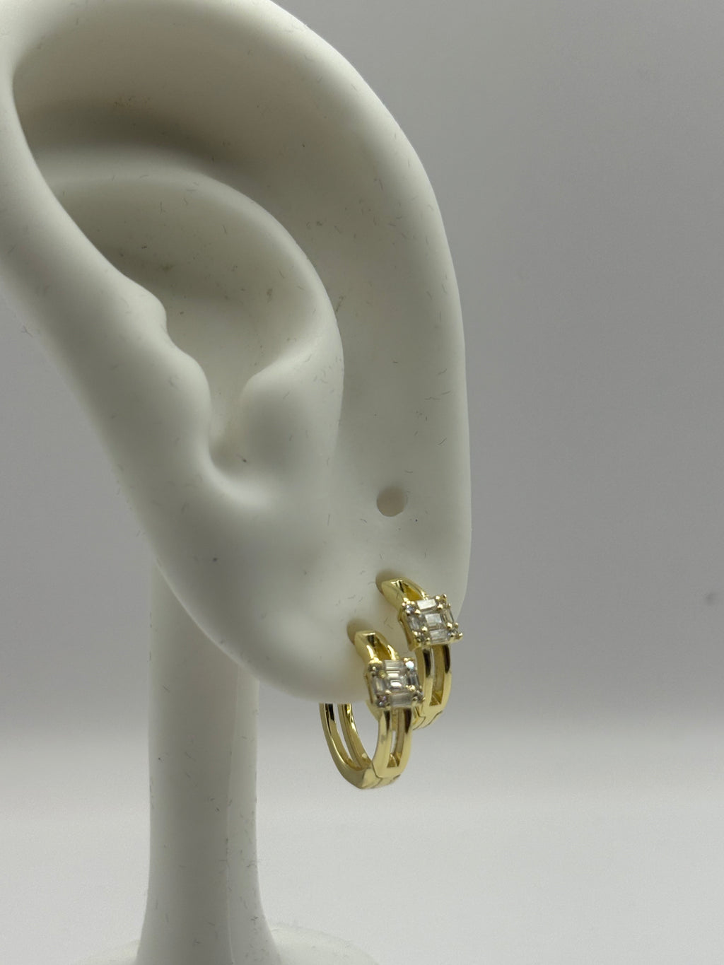 Huggie hoop earrings feature a distinctive open split-shank band and a geometric moissanite cluster design