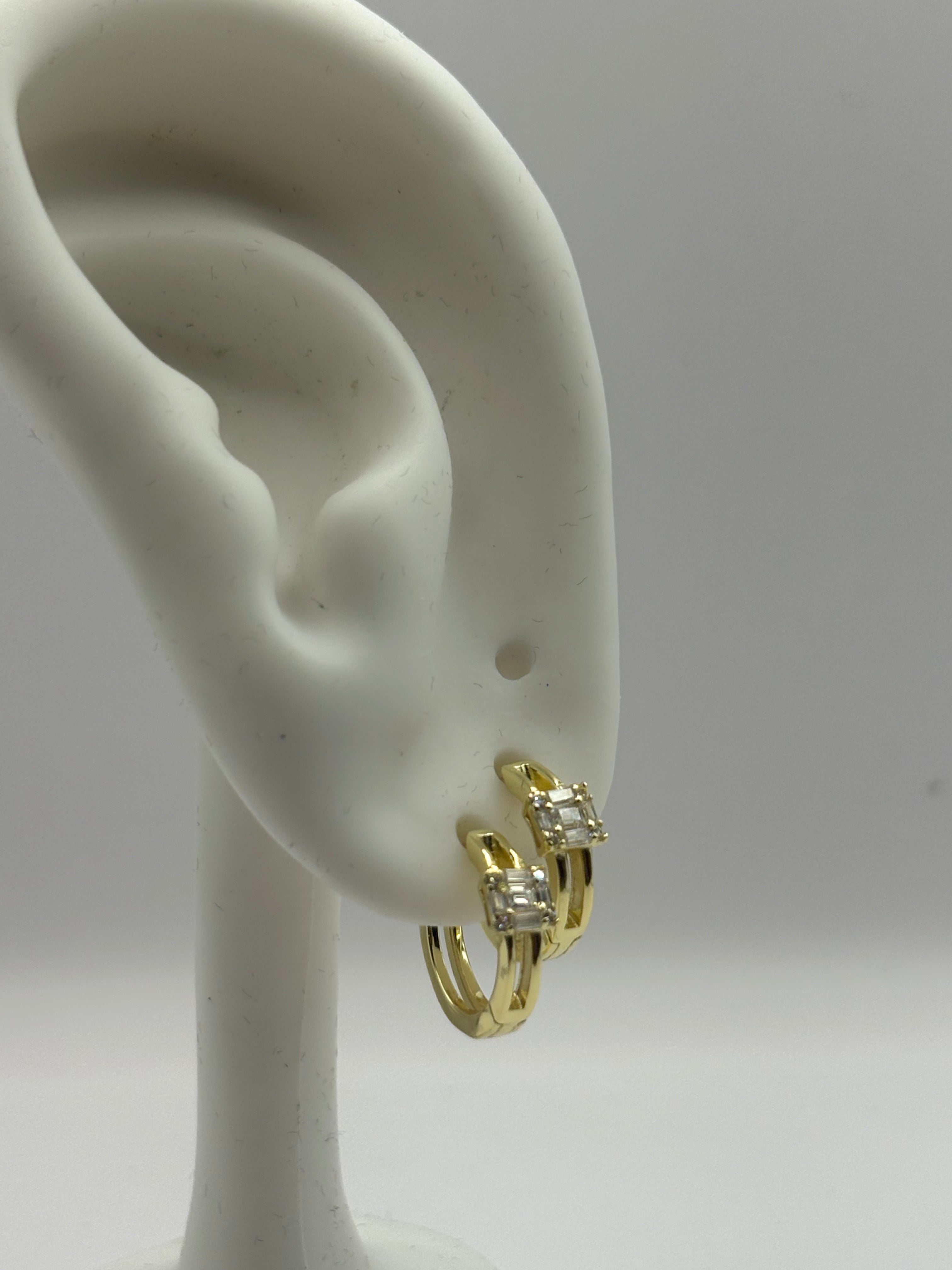 Huggie hoop earrings feature a distinctive open split-shank band and a geometric moissanite cluster design